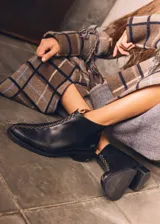 Botín negro de cuero liso, con puntera fina y taco bajo. Presenta costuras decorativas en hilo color crudo y cierre lateral con tirador.
