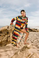 Túnica larga con estampado de rayas horizontales en colores rojo, azul, amarillo, verde y blanco. Tiene cuello camisero, mangas largas y cierre frontal con botones.