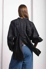 Camisa de lino blanca, de corte oversize, con mangas largas abullonadas, cuello mao y botones. Es más larga en la parte trasera e incluye un tajo en la espalda.