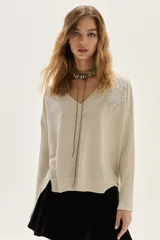 Sweater de tejido de punto con acabado brillante de lurex, escote en V y mangas largas. Presenta detalles de bordados florales en los hombros y un diseño con tajos laterales en el ruedo.