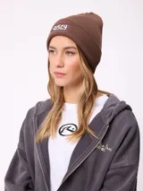 Gorro tipo beanie de tejido de punto acanalado en color marrón, con parche rectangular frontal con el logo de la marca Rusty.