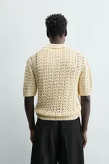 Polo de punto con estructura calada en color beige, confeccionado en algodón. Presenta un calce relajado, manga corta, cuello solapa con abertura frontal y terminaciones acanaladas.