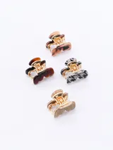 Set de cuatro pinzas pequeñas para el pelo con diseño de mandíbula. Cada pinza tiene un color y patrón diferente: marrón claro, marrón oscuro, gris con patrón pata de gallo y beige con textura de madera.