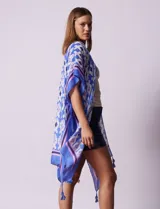 Kimono tejido con estampado abstracto en tonos azules, blancos y violetas. Tiene terminación de ruedo con borlas.