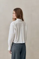 Camisa de algodón blanca de calce relajado y largo cropped, con cuello clásico, cierre frontal con botones y mangas largas.