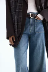 Jean de tiro alto con corte wide leg, confeccionado en denim de algodón con leve elasticidad. Presenta bolsillos de parche frontales, cierre con botón y costuras marcadas a lo largo de las piernas.