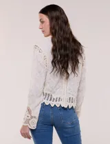Cardigan corto beige de algodón con bordado en relieve, escote redondo y cierre frontal con botones carey. Mangas largas con detalles de encaje crochet y ruedo con terminación en ondas.