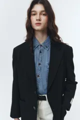 Blazer negro de lana con calce overfit y estética vintage. Presenta cierre frontal de dos botones, bolsillos exteriores y botones de cuerno natural grabados con logo.