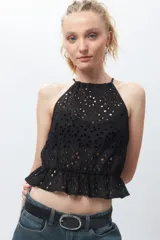 Top blanco sin mangas con cuello halter, bordado con calados y elástico con volado en la cintura.