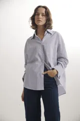 Camisa de corte oversize con diseño de rayas verticales finas, cuello clásico, cierre frontal con botones y bolsillo en el pecho.