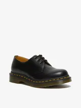 Zapato de cuero negro Dr. Martens modelo 1461, con tres ojales, costuras amarillas y suela con cámara de aire resistente al aceite y a la abrasión.