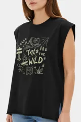 Musculosa color crudo con estampado frontal de paisaje montañoso y texto "EXPLORING Outlands", corte holgado y aberturas laterales en el ruedo.
