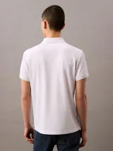 Chomba blanca de corte regular, con cuello clásico y tapeta de dos botones. Presenta un pequeño monograma bordado en el pecho. Confeccionada en poliéster reciclado de secado rápido.