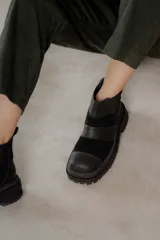 Botas de caña baja con punta cuadrada, confeccionadas en una combinación de cuero liso y gamuza negra. Presentan un diseño de paneles horizontales con costuras visibles y suela track robusta de goma.