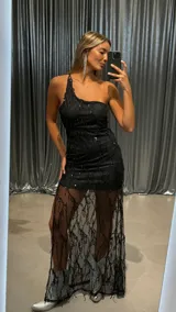 Vestido largo de fiesta color negro con diseño asimétrico de un solo hombro. Presenta una base de minivestido ajustado con una sobrecapa de tela transparente larga decorada con lentejuelas negras en patrones verticales.