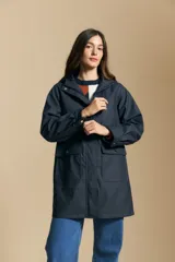 Pilot de largo medio color azul marino, con capucha integrada, cierre frontal oculto y bolsillos aplicados con tapa. Presenta una silueta recta y diseño funcional.