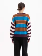 Sweater de punto con diseño de rayas horizontales en tonos marrón, azul, blanco y bordó. Presenta cuello redondo, mangas largas y un pequeño bordado en el pecho. Su corte es holgado y de largo a la segunda cadera.