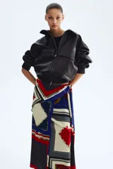 Pollera larga con diseño cruzado efecto pañuelo y brillo sutil. Presenta un estampado geométrico multicolor en tonos azul, rojo y crudo con detalles de cadenas.