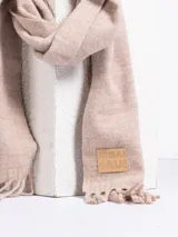 Bufanda de tejido suave en color rosado, con diseño liso y terminaciones con flecos en los extremos. Incluye una etiqueta de cuero sintético con el logo de la marca en uno de los bordes.