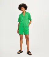 Camisa de manga corta confeccionada en mezcla de viscosa y lino, con cuello camisero en pico, cierre frontal con botones geométricos y bolsillos delanteros.