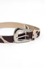 Cinturón de cuero con estampado animal print tipo vaca en tonos marrón y beige, con hebilla metálica plateada de estilo western.