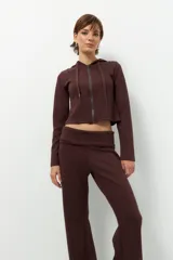 Camperita deportiva color marrón oscuro, ajustada al cuerpo, con capucha y cierre frontal a tono. Presenta costuras verticales que estilizan la figura.