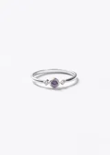 Anillo de plata 925 con piedra central de zirconia color violeta y dos piedras laterales pequeñas de zirconia transparente.