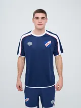 Remera deportiva de entrenamiento Umbro del Club Nacional de Football, color azul marino con detalles en blanco y líneas rojas en los hombros. Cuenta con el logo de la marca y el escudo del club en el pecho.