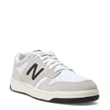 Championes urbanos New Balance modelo 480 Court, con diseño de inspiración retro. Presentan una combinación de cuero blanco perforado en la puntera y paneles laterales con superposiciones de gamuza en tono gris claro. Incluyen el logo 'N' característico en color negro en los laterales, cordones blancos y una suela de goma con base negra.