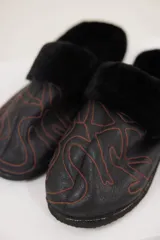 Pantuflas de cuero negro con interior de piel sintética, diseño con bordados decorativos en color naranja y suela plana.