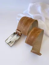 Cinto de cuero color camel con forro de cuero y hebilla rectangular de guampa con borde metálico trenzado. Cuenta con broche suizo intercambiable.