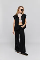 Pantalón jean de tiro medio, color negro, de corte amplio y silueta extra wide leg. Presenta diseño clásico de cinco bolsillos, cierre frontal con botón y cremallera, y detalle de tachas metálicas aplicadas a lo largo de los laterales.
