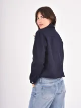 Chaqueta corta de paño en color azul oscuro, con cuello camisero, cierre frontal con botones metálicos dorados y dos bolsillos frontales con solapa.