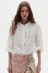Camisa blanca de algodón, de corte clásico y atemporal, con cuello mao, mangas abullonadas y detalle de volados en la botonera frontal oculta.