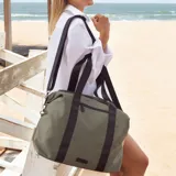 Bolso deportivo color gris claro, con cierres y correas negras. Cuenta con dos asas superiores, bolsillo frontal con cierre y correa extensible ajustable.