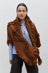 Chal de lana color marrón con diseño envolvente, decorado con volados aplicados que recorren toda la prenda, aportando textura y movimiento.