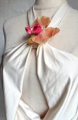 Top color crema o amarillo pálido, estilo halter con cuello atado y escote pronunciado en V con drapeado frontal. El cuello está adornado con una flor de orquídea en tonos amarillo, naranja y rosa.