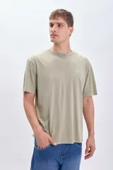 Camiseta manga corta oversize color verde con estampado de una pieza de rompecabezas con una flor en su interior y la palabra 'Island' debajo.