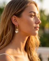 Aros tipo argolla en acero dorado con dije colgante que combina un delfín y un corazón con incrustación de nácar.