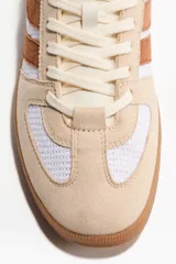 Calzado deportivo con exterior tejido blanco y detalles en gamuza marrón y beige, con cordones frontales y suela de goma.
