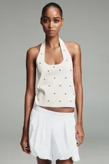 Top de punto negro con cuello halter y escote redondo, decorado con tachas metálicas plateadas distribuidas por toda la prenda.