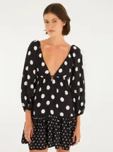 Vestido corto con estampado de lunares blancos sobre fondo negro, con escote profundo en V, mangas largas abullonadas y falda en capas con acabado en marias.