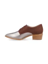 Zapato tipo oxford con cordones, combinando cuero metalizado plateado en la puntera y gamuza marrón en la parte trasera. Cuenta con un taco bajo de madera y cierre mediante cordones.