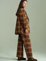 Blazer de corte oversize con estampado de cuadros en tonos marrones y ocres. Presenta solapas de terciopelo negro, cierre frontal con dos botones y bolsillos delanteros. El interior está forrado en satén.