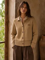 Cardigan de punto color tostado con cuello polo, cierre frontal de botones y detalles de costuras decorativas en el ruedo y los puños.