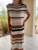 Vestido largo de tejido de punto, con rayas horizontales en tonos tierra, azul y blanco. Presenta cuello redondo, mangas cortas caídas y aberturas laterales en el ruedo.