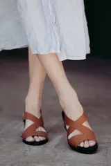 Sandalias de neopreno color marrón con tiras cruzadas en el empeine y puntera abierta. Cuentan con un taco irregular de 6 cm de altura y plantilla de cuero.