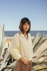 Camisa de seda color amarillo pastel con silueta relajada, cuello camisero, cartera frontal con botones, mangas largas y puños amplios con múltiples botones. Presenta terminación elastizada que genera un sutil efecto abuchonado.