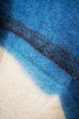 Bufanda tipo manta suave con diseño de bloques de color en tonos beige, azul y marrón, terminada con flecos en los extremos.