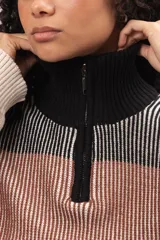 Buzo de tejido de punto con diseño a rayas horizontales en tonos tierra, negro y crema. Presenta cuello alto con cierre frontal parcial, mangas largas con puños ajustados y corte holgado.